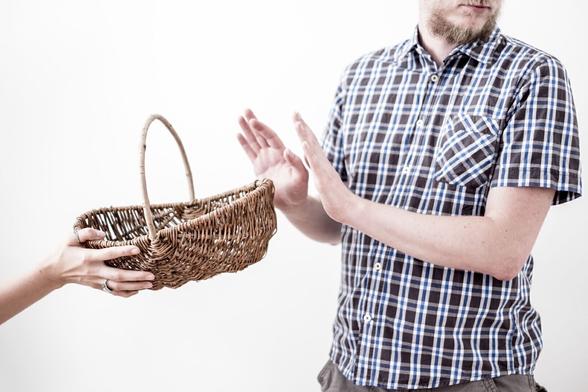 Ein Korb wird von einem Menschen an sein Gegenüber gereicht. Vor der ersten Person ist lediglich eine zarte Hand mit Ring am Ringfinger zu sehen. Die zweite Person lehnt den Korb mit erhobenen Händen ab.