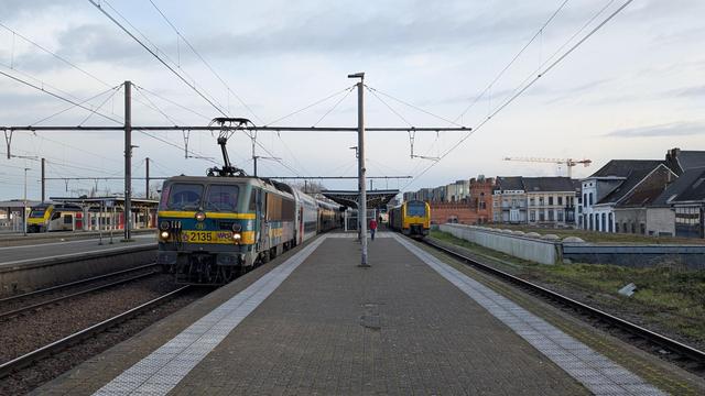 An elevated island platform with dark-grey bricks, a NMBS/SNCB class 21 locomotive pulling M5 double decker coaches on the left, two NMBS/SNCN class 41 DMU on the right