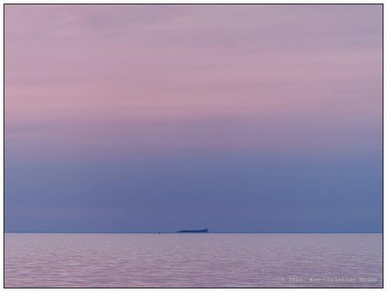 Ruhevolle Ostseeküste bei Hohenfelde im nördlichen Kreis Plön, die Horizontlinie verläuft im unteren Bildviertel, Wasser und Himmel sind einheitlich in sanft-pastelligen rosa-, violett- und Blautönen gefärbt und bilden so einen einheitlichen Raum, mittig ein Schiff am Horizont.