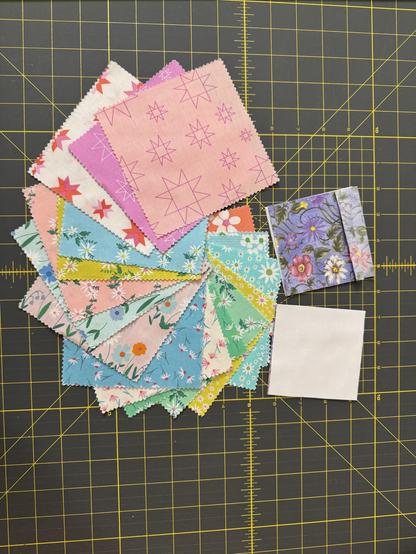 Pile of several different color fabrics, some in 5 in by 5 inch squares and some on 3 1/2 inch squares.  Colors include pink, purple, yellow, blue, green, and white.