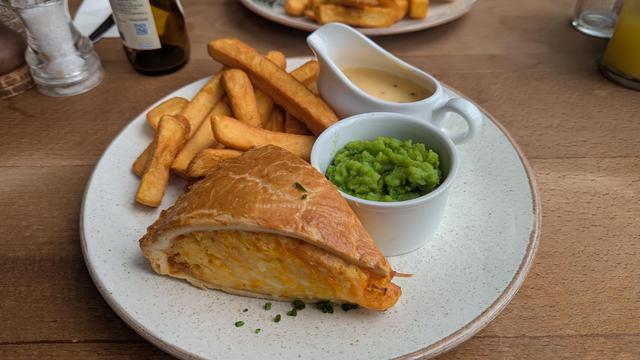 A large piece of the 3 cheese and onion pie with crispy shortcrust pastry, a little dish of mushy peas, a small jug of cheese & chive sauce and some crispy chunk chips.