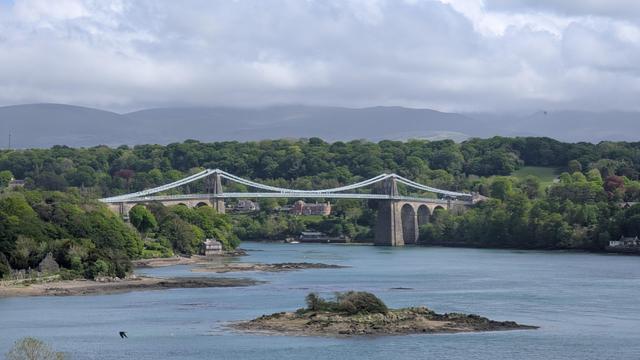 A view from a hill looking down towards the Menai Suspension bridge which is nearly 250yrs old. It recently underwent a multi million pound refurbishment after serious faults were discovered during an inspection in 2022 that closed it for months. There are only 2 routes on and off the island of Anglesey and one was closed for the better part of 4 months whilst emergency supports were installed. For a further few months it was only open to pedestrians, motorcycles and cars... and about 3yrs later, nothing larger than a van is ever allowed to cross it again.