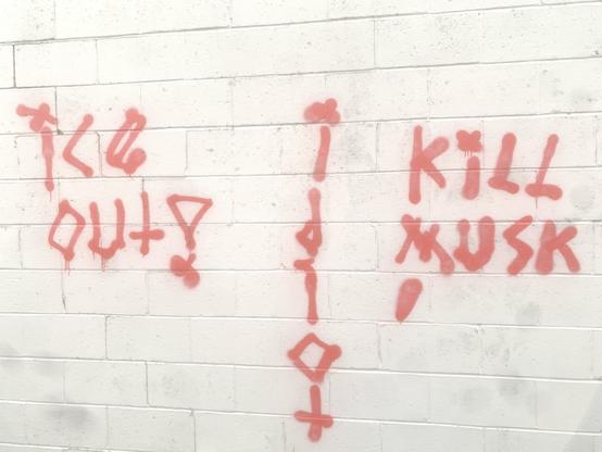 “Ice Out” “Kill Musk” graffiti in red spray paint on a Gray brick wall
