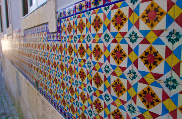 colorfulorange, blue, white, black, green, and yellow  tiles stretch in a repeating decorrative pattern along a wall toward a reflection of the sun