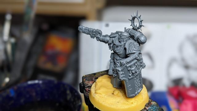 An unpainted grey Space Marine Captain with Deathwatch shoulder pad and shield standing on a yellow base.