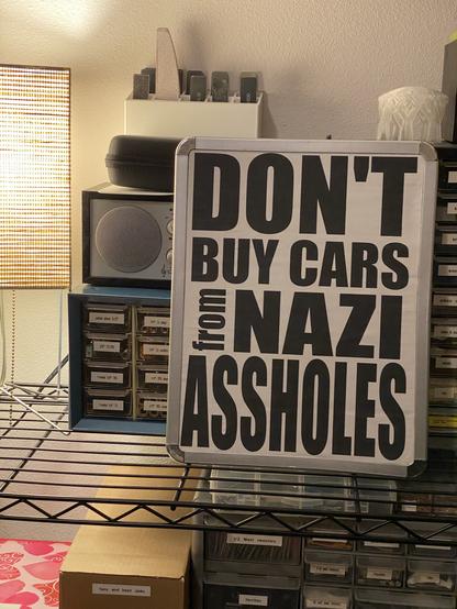 the "don't buy cars from nazi assholes" word-art printout pasted to the back of the emergency-purchase $1 whiteboard from Saturday's Tesla picket protest.
