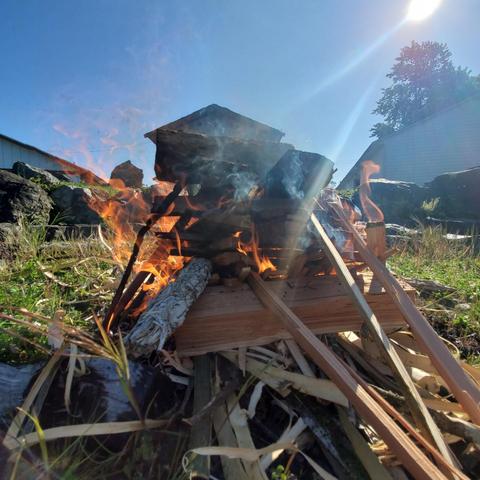 A outdoor fire burning with big sage smudge stick on the lower left. Esquimalt First Nation buildings are in the background.
