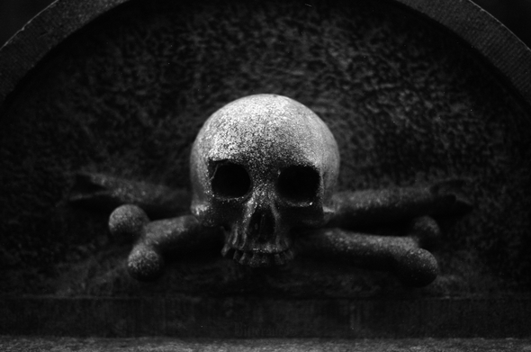 Quite dark black and white film photo of a stone skull and crossbones on an old gravestone