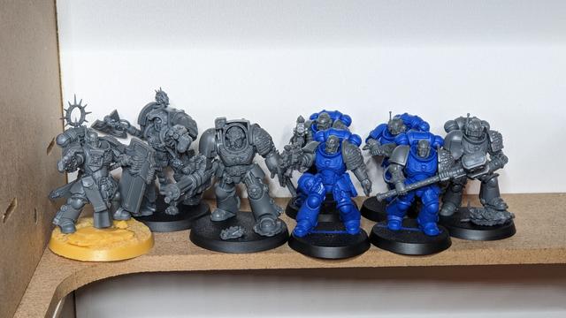 8 unpainted Space Marines standing close together. Four of them have blue bodies.