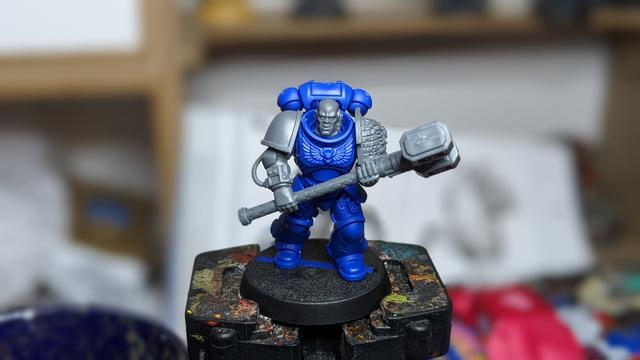 An unpainted Space Marine with blue body and an Energy Hammer