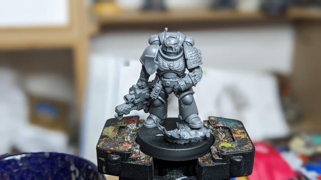 An unpaited grey Space Marine in an eased pose carrying a Heavy Bolter Flamer.