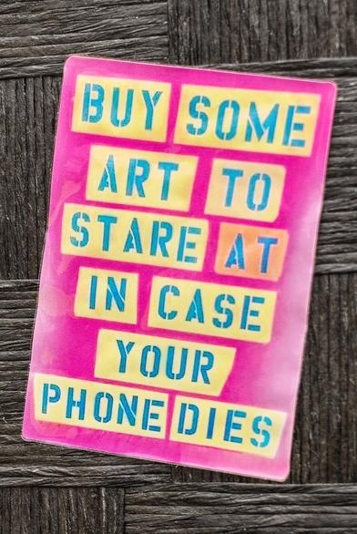 Laminated card that says, "BUY SOME ART TO STARE AT IN CASE YOUR PHONE DIES"