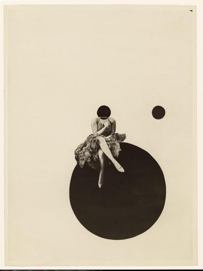 The image features a surreal composition on a light beige background. A figure, dressed in a textured, ruffled dress, is seated with legs crossed atop a large, solid black circle located near the bottom right of the image. The figure's head is a smaller black circle which aligns with their neck, giving an abstract, faceless appearance. Above and to the right of this, there is another small black circle floating in the negative space, creating a sense of balance within the composition. The minimalist