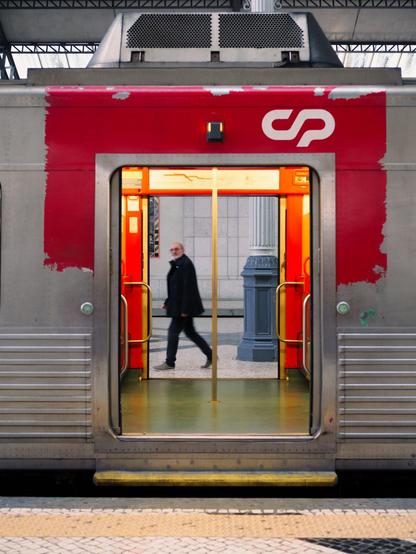 A man walks past on the opposite side of a train wagon. We see him through the open doors of the train as he walks briskly on the platform while glancing at us.