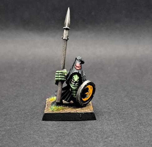 A Warhammer Fanatasy Night Goblin with a Spear and Shield. He has green skin and is wearing a black robe. On the shield is a yellow crescent moon.
