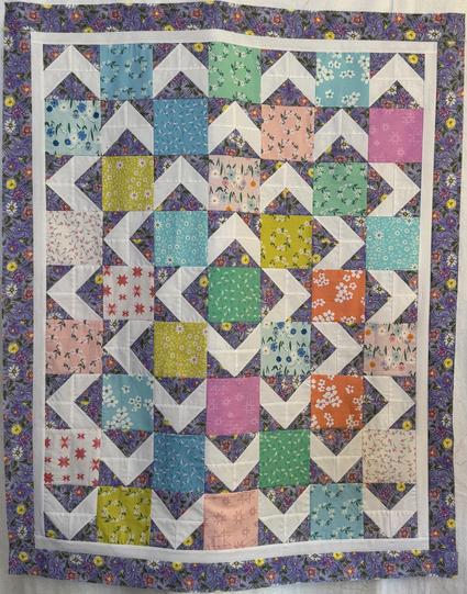 Quilt top with mostly pastel colors with a series of what looks like outlines of squares in white underneath patches of color.