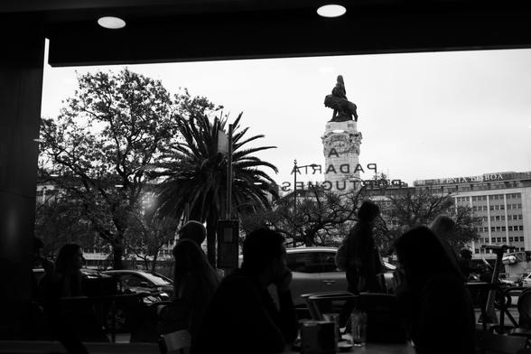 BW picture of the Marques de Pombal statue, as seen through the window of a bakery.