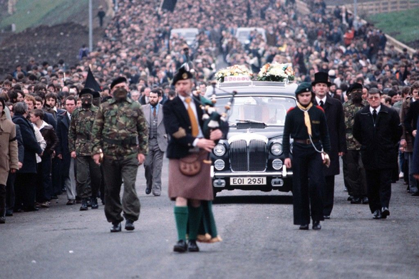 A piper walking ahead of a hearse bearing Bobby Sand's coffin.