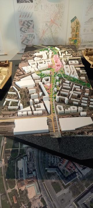 Vor einer Karte der St. Petersburger Straße, die an der Wand hängt, steht ein Modell ebendieser Straße mit neuer Bebauung, Radinfrastruktur und deutlich mehr Begrünung.