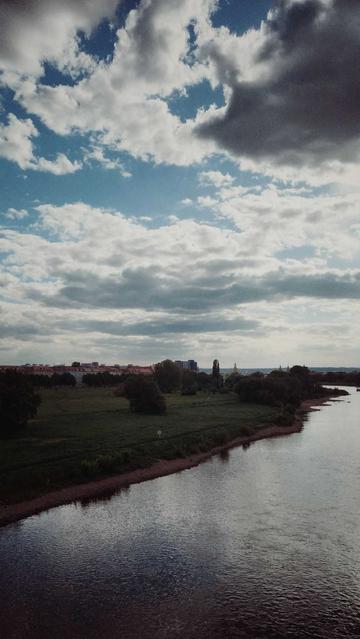 Wild sky above a quiet river. Meadows and distant houses on the left side.