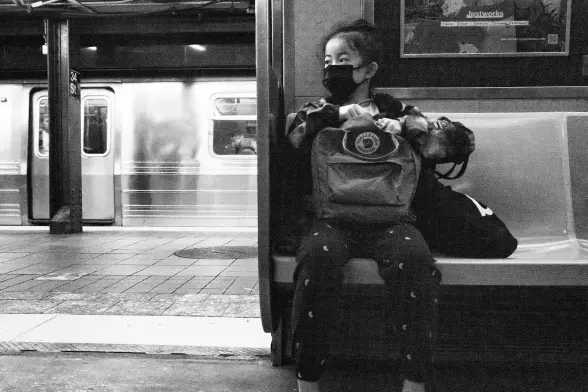 A girl sits in a subway train wearing a mask