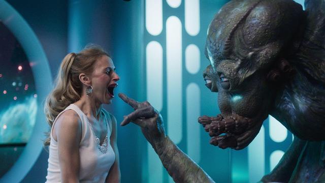 An alien reaches a finger out to a woman whose mouth is open