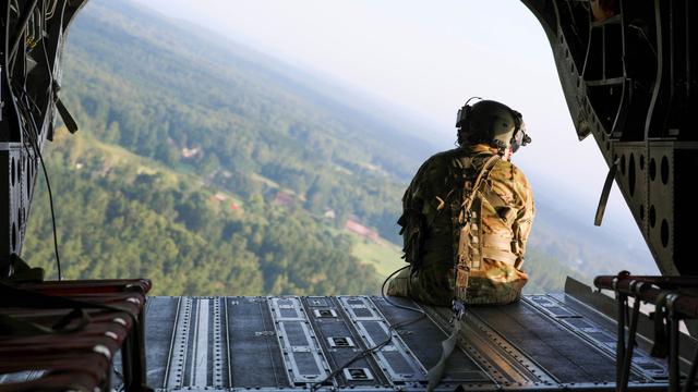 A US soldier sits on the edge of a helicopter looking out.
