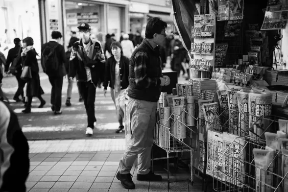 A man in front of a newspaper stand in a busy street