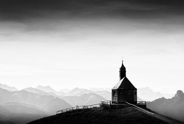 black and white. landscape format. In the foreground the wallberg chapel. in the background a wide view of the mountain landscape of the foothills of the alps.