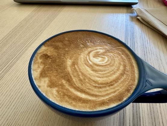 Small blue coffee cup filled with a frothy cappuccino sitting on a light brown wooden table