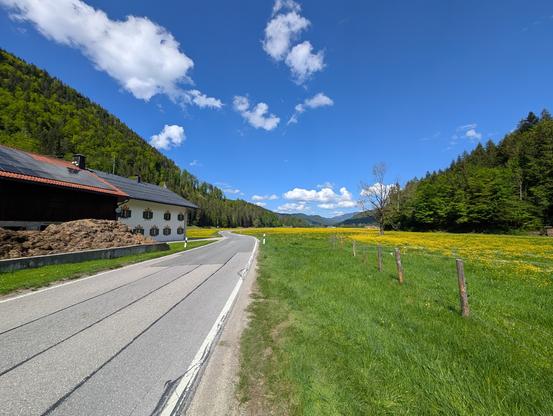 Blühende Jachenau unter weiß-blauem Himmel.
Am Straßenrand ein großer Misthaufen.