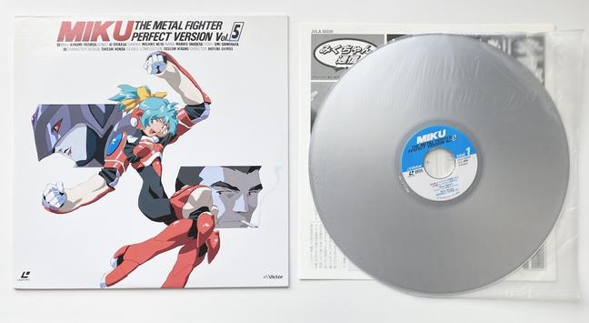 A photo of an anime laserdisc and its cover.
The cover shows an illustration of Miku, a young female wrestler with turquoise hair and a black leotard with red armor