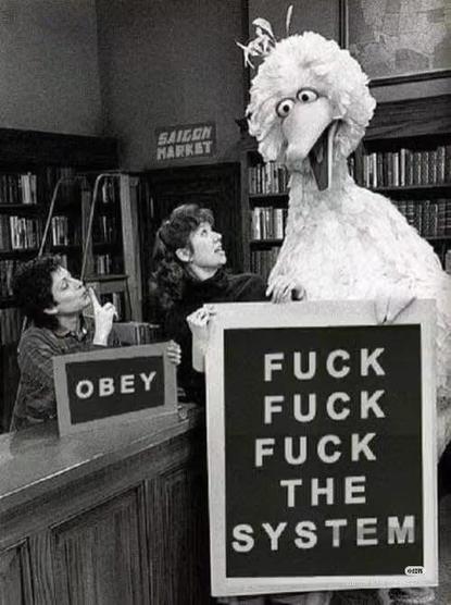 A woman making the hushing hand gesture holding a sign that says "obey" next to Big Bird, who is holding a sign that says "Fuck, Fuck, Fuck the System."