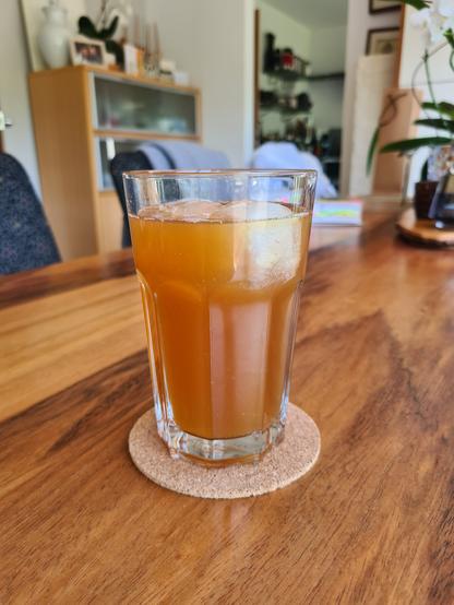 Ein hellbeiges Getränk mit Eis in einem Glas auf einem Holztisch