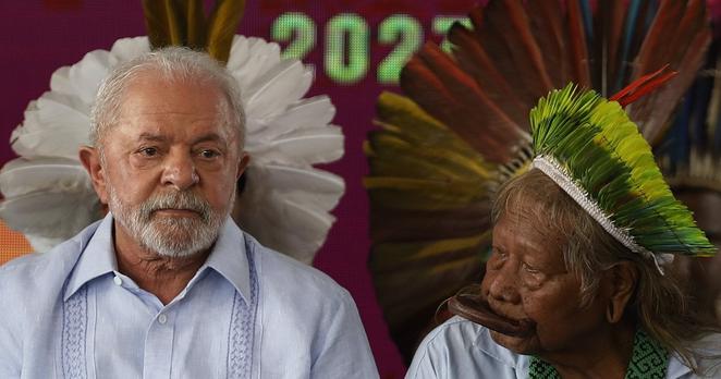Präsident Lula mit dem Kayapo Anführer Raoni vor einer Wand mit Fotos von Federschmuck