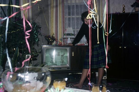 Ein Wohnzimmer, in dem offenbar kürzlich eine Party stattfand, ein paar Luftschlangen, in der Mitte ein Fernseher