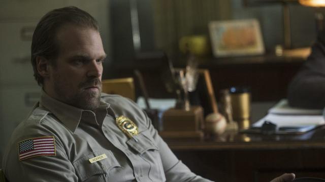 David Harbour wears a police uniform and sits at a desk in 'Stranger Things'.