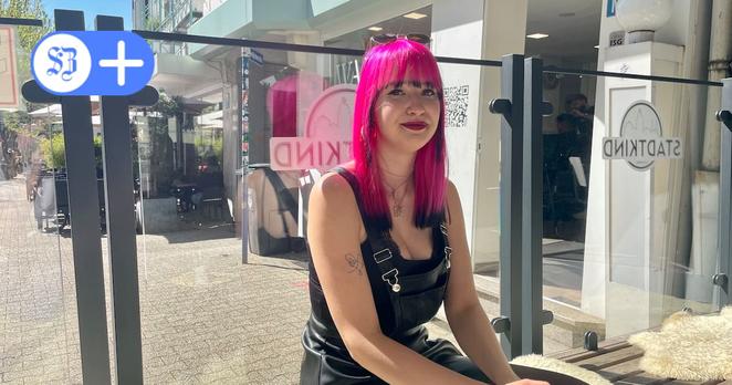 Foto von Lilli Marleen Paulmann im Außenbereich des Siegener Cafés Stadtkind. Sie trägt eine schwarze Latzhose aus Leder und pinke Haare.