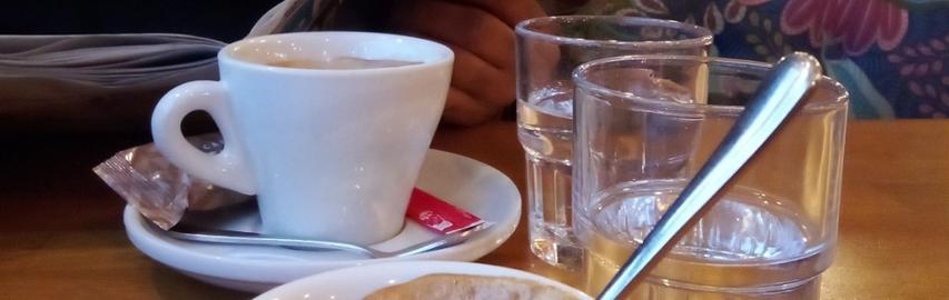 Une tasse de café blanche posée sur une soucoupe blanche la même couleur. Deux verres d'eau à moitié rempli se trouve l'un à côté de la tasse, l'autre au premier plan.