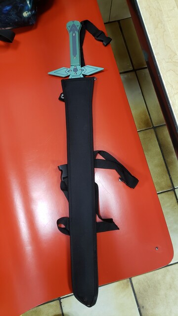 A greenish-grey costume sword, origins & reference unknown, in a black synthetic vinyl sheath, straps & snaps to secure it to one's body or bundle.