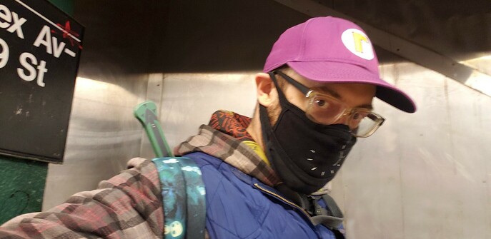 Greenish-grey costume sword, origins & reference unknown, strapped to the back of its new owner, a suave-if-nerdy latter 40-something ostensibly Caucasian man, wearing an avocado plaid hooded jacket, a blue Star Wars Millennium Falcon pillow vest, a Princess Mononoke backpack, a Waluigi cap, a black About Time facemask, and black & clear framed glasses, at the 59th St & Lexington Ave N/R/W platform of the NYC MTA.