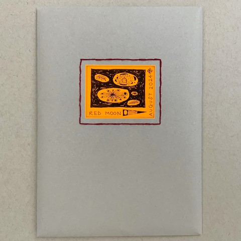 An envelope made from mushroom-colour paper, with a sewn frame in red thread, and inside the frame is a sticker with illustrations of leaves and flowers. 