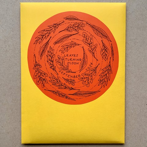 A handmade envelope with a circular sticker on the front that has illustrations of autumn leaves spinning around. 