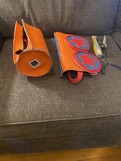 Assembling parts for a star tube/duffle shaped vinyl bag, with plier stapler and pliers. Orange, red, and blue vinyl pieces.