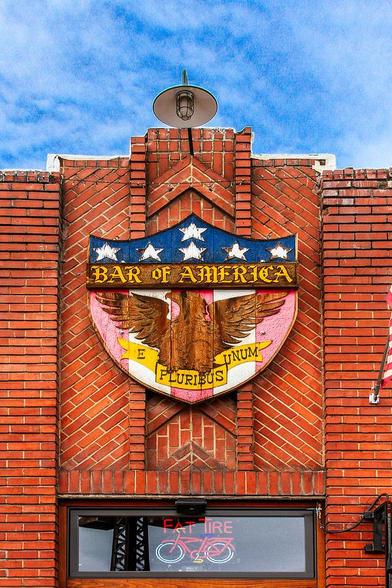 Bar Of America

This is an image of the front facade of the Bar of America located in Truckee, California.
The faded coat of arms is what caught my eye. That and the fact that they serve Fat Tire Beer.
The coat of arms has a banner crossing the front with the name "Bar of America". Above the banner are six white stars on a blue background. Below the banner is a Bald Eagle and another banner with "E Pluribus Unum" on it. The background for this is red and white stripes.
The brick exterior has different patters at angles. The lone window has a neon Fat Tire sign in it. The sky is partly cloudy with high light clouds.