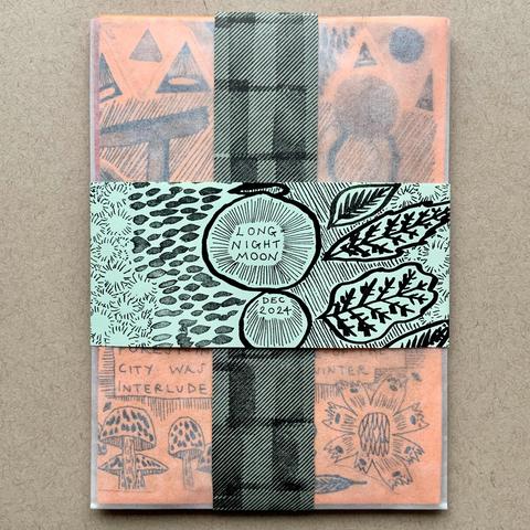 A set of four zines/comics, packaged in a glassine envelope, with strips of patterned paper over the top.