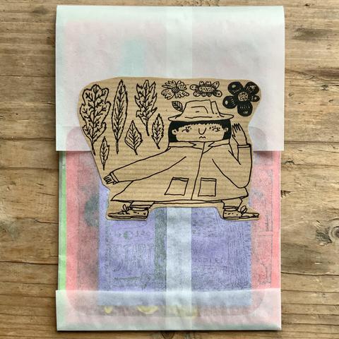 The back of the glassine envelope that has a sticker of detective Tso listening intently, surrounded by leaves and flowers. 