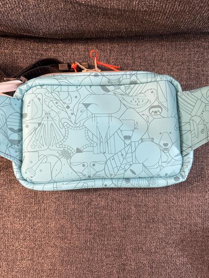 Back of belt bag made from light turquoise Charley Harper animal character print vinyl, with tan zippers, orange zipper pulls, and violet stitching