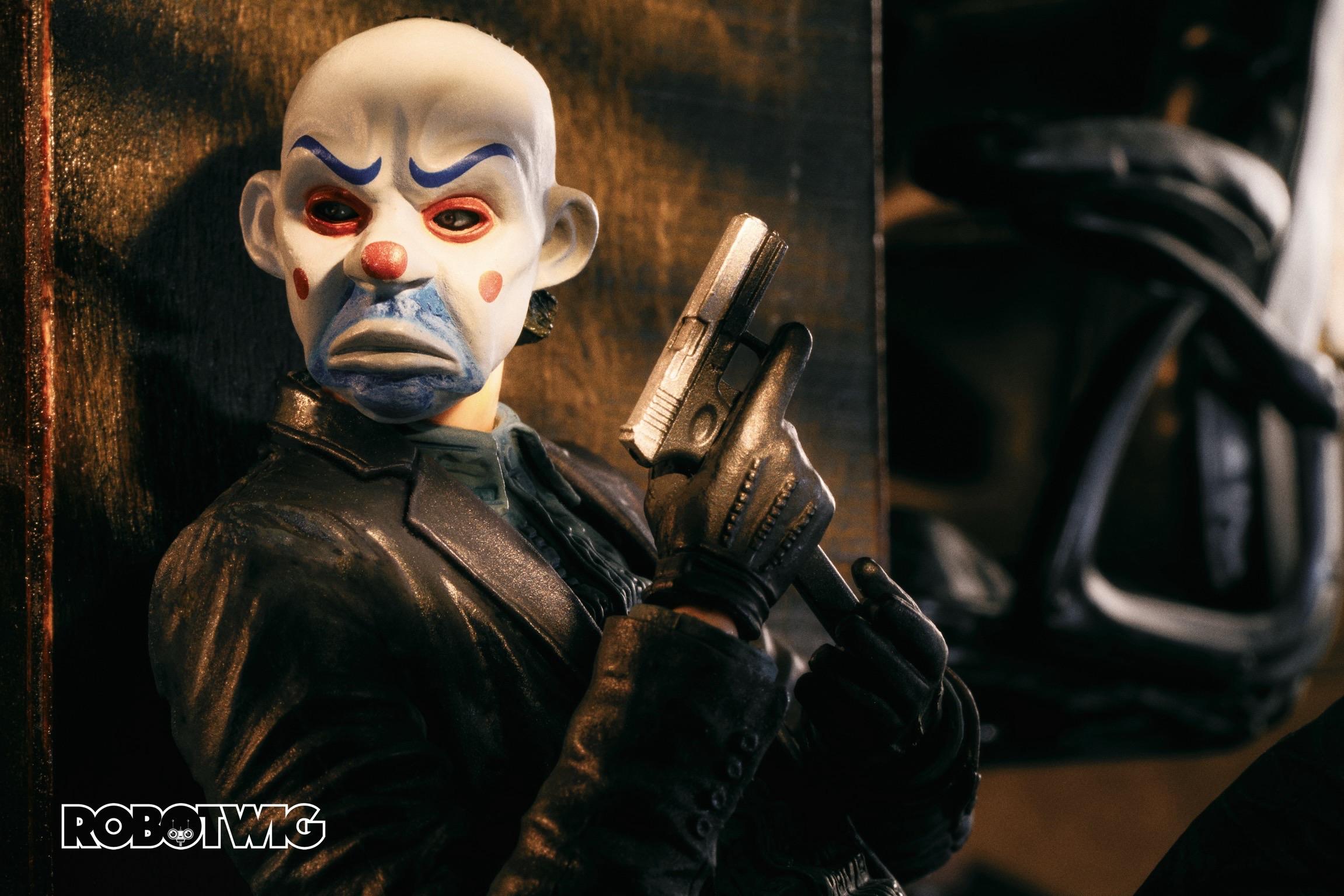 The Joker in a clown mask hides begins a table reloading a gun in a bank that he and his team are robbing