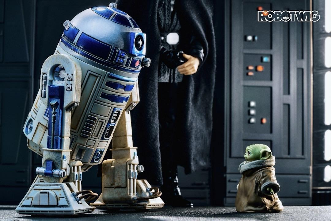 R2D2 and Luke Skywalker meet Grogu who stands alone looking up at them both.